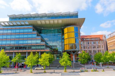 Berlin, Almanya - 16 Ağustos 2025: Berlin 'deki Linkstrasse 6 binasının mimari görünümü, parlak cam cepheler ve yeşillik ortasında çarpıcı sarı silindirik bir yapı.