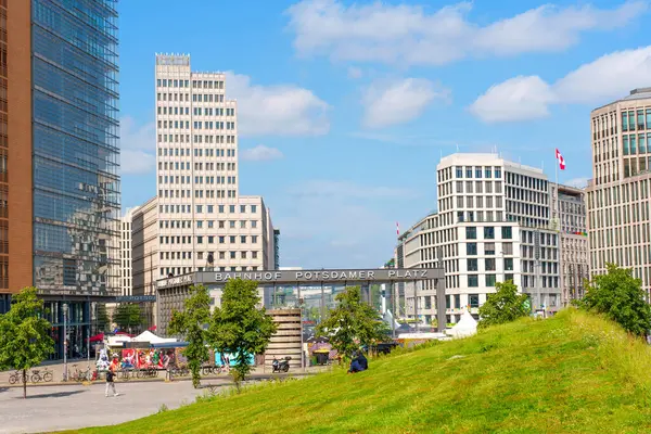 Berlin, Almanya - 16 Ağustos 2025: Modern mimari, yeşil çimenlik alanlar ve Berlin 'deki kentsel yaşamı yansıtan açık mavi bir gökyüzü içeren hareketli Potsdamer Platz manzarası.