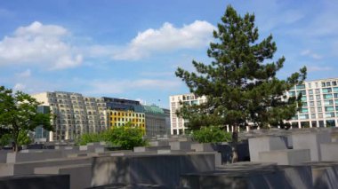 Berlin, Almanya - 31 Mayıs 2025: Berlin, Almanya 'da ağaçlar ve modern binalarla çevrili, mavi gökyüzünün altında gri beton levhaların yer aldığı Avrupa Öldürülen Yahudileri Anma Töreni.