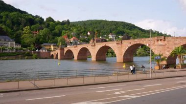 Heidelberg, Almanya - 21 Haziran 2025: Heidelberg, Almanya 'daki Karl-Theodor Köprüsü Kapısı' nın geniş açılı görüntüsü, güneşli bir günde tarihi mimari ve huzurlu nehir batışını gözler önüne seriyor..