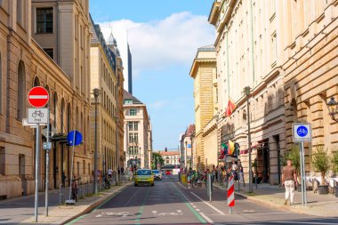 Berlin, Almanya - 16 Ağustos 2025: Açık mavi gökyüzü altında tarihi binalar, bisiklet şeritleri ve canlı şehir yaşamının karışımından oluşan hareketli bir şehir sokağı Berlin 'de.