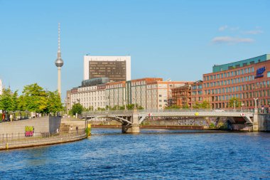 Berlin, Almanya - 16 Ağustos 2025: Berlin 'de ikonik televizyon kulesi, modern binalar ve açık mavi gökyüzünün yer aldığı manzaralı nehir manzarası.
