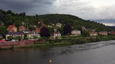 Almanya 'nın Heidelberg kentindeki Neckar Nehri' nin sakin manzarasında açık mavi gökyüzünün altında büyüleyici evler ve yeşil tepeler sergileniyor..