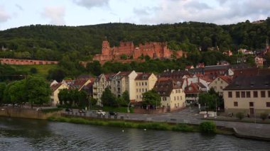 Heidelberg, Almanya - 21 Haziran 2025: Heidelberg Şatosu, Neckar Nehri, gezinti alanı, evler, kavşaktaki arabalar ve yeşil tepeler, tarihi şehir manzarası ve manzaraya odaklı.