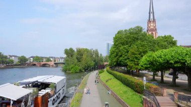 Frankfurt, Almanya - 10 Haziran 2025: Yürüyen, koşan ve bisiklet süren insanların bulunduğu Frankfurt liman sahnesi, kentsel etkinlik ve nehir manzarasına odaklanmış.