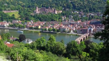 Heidelberg, Almanya - 21 Haziran 2025: Heidelberg Şatosu ve Neckar Nehri üzerindeki Eski Köprü manzarası, köprüde yürüyen turistler ve nehirde turistlerle dolu açık bir tekne.