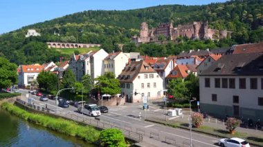 Heidelberg, Almanya - 21 Haziran 2025: Heidelberg Şatosu, tarihi binalar ve bir grup ziyaretçiyi taşıyan açık tepeli bir turist otobüsü olarak nehir kıyısı.