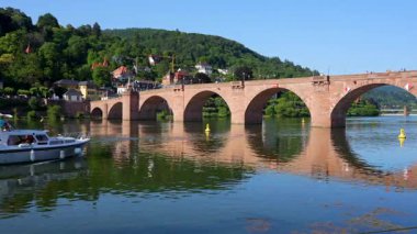 Heidelberg, Almanya - 21 Haziran 2025: Heidelberg, Almanya 'nın geniş açılı çekimi, açık mavi gökyüzünün altında eski köprüyü ve Neckar Nehri' nde bir tekneyi gösteriyor.