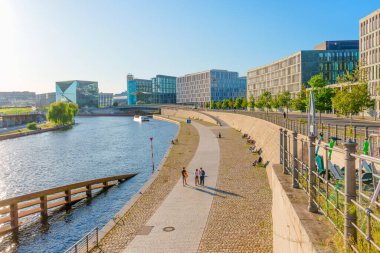 Berlin, Almanya - 16 Ağustos 2025: Berlin 'deki Spree Nehri' nin geniş açılı görüntüsü, çağdaş binalar ve ziyaretçilerle dolu canlı bir rıhtım geçidi.