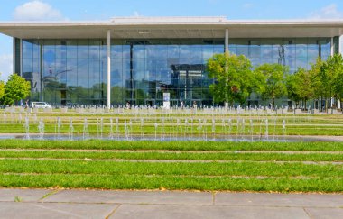 Berlin, Almanya - 17 Ağustos 2025: Çağdaş mimariyi yansıtan, fıskiyeli yeşil bir parka bakan çarpıcı modern cam bina.