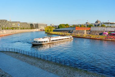 Berlin, Almanya - 16 Ağustos 2025: Spree Nehri 'nde gezinen tekne, nehir ile Berlin' in şehir manzarası arasındaki güzel etkileşimi vurguluyor..