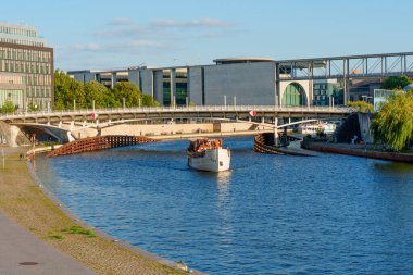 Berlin, Almanya - 16 Ağustos 2025: Modern Berlin mimarisi tarafından çerçevelenmiş Spree Nehri 'nde seyahat teknesi, kentsel etkinlikleri resmediyor.