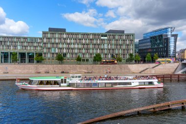 Berlin, Almanya - 17 Ağustos 2025: Berlin 'de modern mimarinin yanında Spree Nehri boyunca süzülen yolcularla dolu yelkenli tekne.