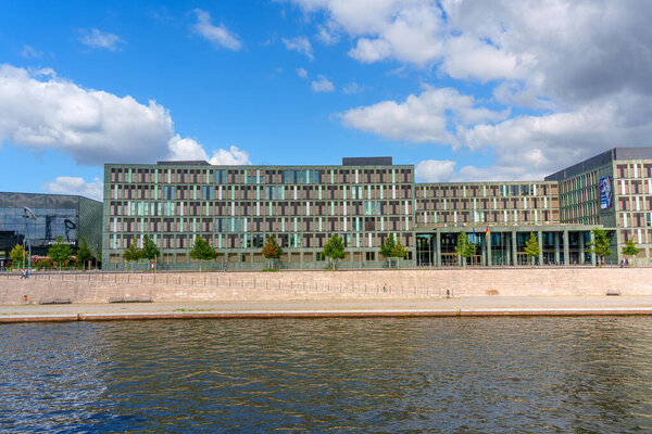 Берлин, Германия - 17 августа 2025 года: Современный дизайн здания Федерального министерства образования и исследований в Берлине с отражающими окнами вдоль набережной под голубым небом.