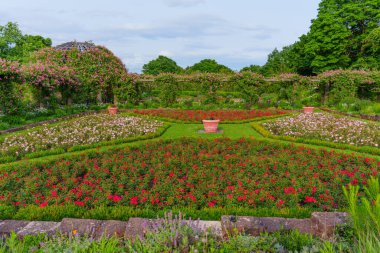 Geometrik desenlere göre düzenlenmiş renkli çiçek yatakları bakımlı bir parkta yemyeşil ile çevrili..