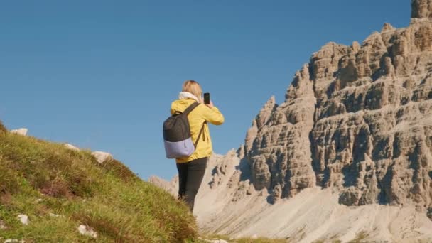 ブロンドの女性はスマートフォンのカメラで山の風景を撮影します 女性観光客はTre Cime Lavaredoに近いイタリアアルプスの山々を賞賛します — ストック動画