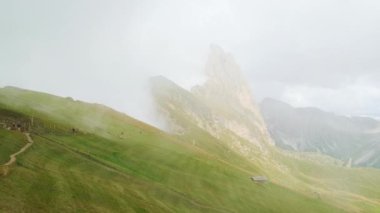 İtalyan Alpleri 'nde Seceda Dağı' nın beyaz bulutlarıyla kaplı. Yeşil yamaçlardan oluşan dağ manzarası. Turistler hava manzaralı yolda duruyorlar