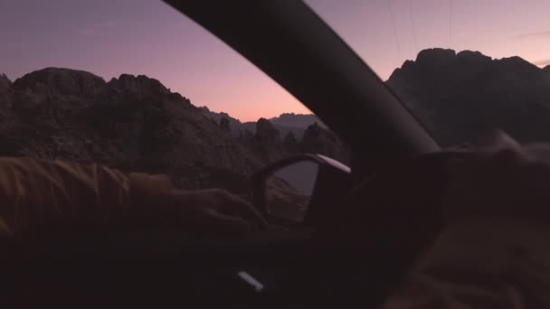 男は日没時にアルプスの山の中で車を運転する ドライバーは車の窓から手を出し 風がスリップし 指の間のスライドがスローモーションを閉じます — ストック動画