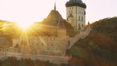 Büyük gotik şato Karlstejn gün batımında parlak güneş ışığıyla aydınlatılıyor. Antik kale Çek Cumhuriyeti hava görüşünde turistleri cezbediyor