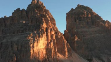 Çıplak kayalık dağların devasa sivri tepeleri mavi bulutsuz gökyüzünün altında sıralanır. Gün doğumunda Tre Cime di Lavaredo 'nun manzarası.