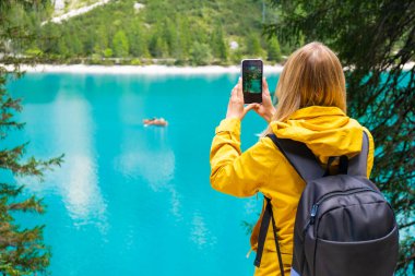 Turist, Dolomite dağlarındaki çarpıcı göl Braies 'in turkuaz su ve ahşap botlarla fotoğrafını çekiyor.. 