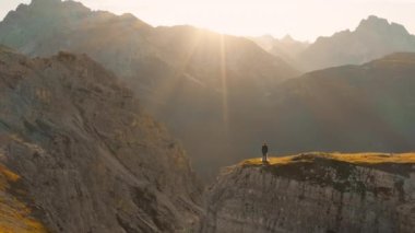 Gelin ve damat gün batımında Tre Cime di Lavaredo 'da uçurumun kenarında dururlar. Arkasında orman vadisi manzarası olan kayalık bir dağ yığını.