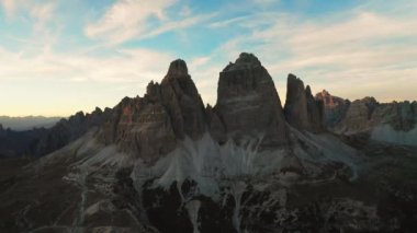 Gün batımında Tre Cime di Lavaredo 'nun yüksek taş kolonları. Mavi gökyüzünün altında, beyaz bulutlar ve hava manzaralı savaş benzeri zirveler.