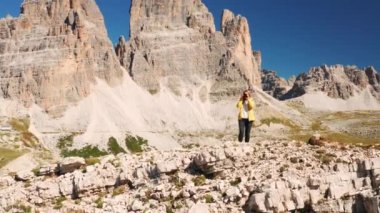 Dişi turist, dağ zirvelerini kamerayla çekiyor. Sarışın kadın, Lavaredo 'nun Üç Tepesi hava manzarasının yakınındaki kayalık dağlık arazide tepede duruyor.