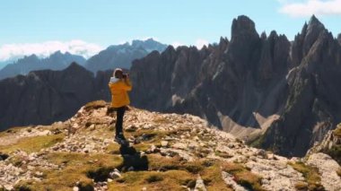 Kadın panoramik gözlem noktasında durup Lavaredo 'nun Üç Tepesi ve Kanyon' u kamerayla çekiyor. Dişi turist, dağ manzarasına bakıyor.