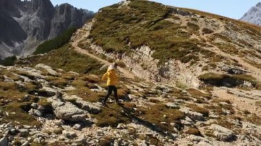Dişi gezgin kayalık yamaçtan yere doğru gidiyor. Sarışın kadın, yüksek Tre Cime di Lavaredo dağları manzaralı kanyon kenarında yürüyor.