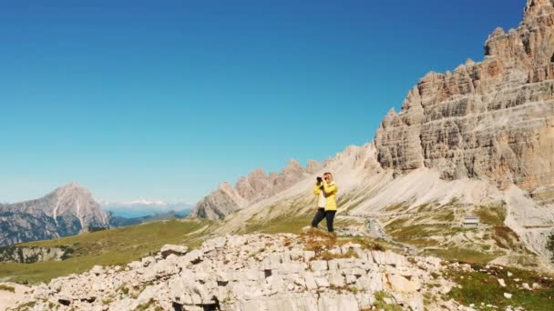 Блондинка Фотографирует Горные Вершины Стоящие Высоком Каменистом Холме Женщина Туристка — стоковое видео