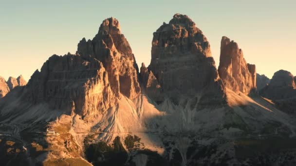 日の出の青空の下で高い山の風景 ライトアップされた岩の斜面とラバレドの3つのピークの灰色の砂のベースで覆われている航空ビュー — ストック動画