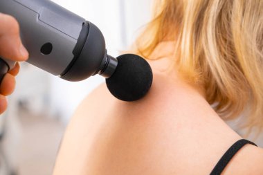 Masaj silahı kullanarak bir kadının boynuna masaj yapan bir terapist. İyileşmek için fizik tedavi. 