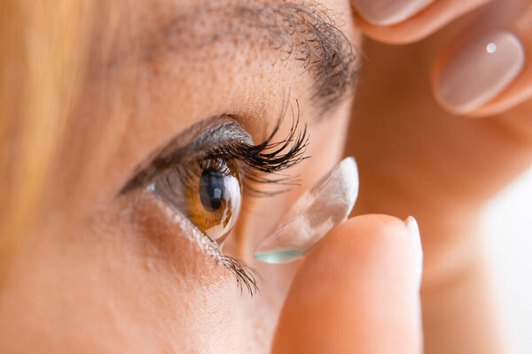 Young woman putting contact lens into her eye, close up.