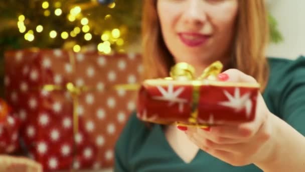 緑色のドレスを着た女性は 背景にライト ラップされたプレゼント クリスマスツリーをプレゼントします — ストック動画