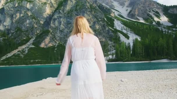 金发女子在沙滩上奔跑 奔向碧眼碧眼的碧眼湖 身着白色长裙的女士凝视着意大利的自然后视镜慢动作 — 图库视频影像