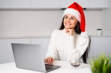 Noel Baba şapkalı mutlu kadın Noel ya da yeni yıl tatili hayal ediyor. Partiden önce not defterini kullanan bir kadın evde çalışıyor.. 