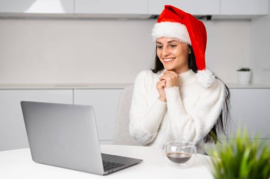 Noel Baba şapkası takan gülümseyen bir kadın Noel 'de aile veya arkadaşlarıyla görüntülü görüşme yapıyor. Mutlu Noeller ve yeni yıl.