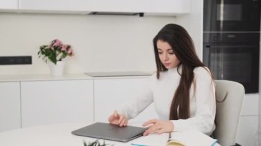 CHARLOTTE, Birleşik Devletler - 19 Kasım 2022: genç kadın ödevlerine devam etmek için MacBook 'u açıyor. Bayan öğrenci şık bir mutfakta masa başında modern bir dizüstü bilgisayar üzerinde çalışıyor.