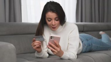 Mutlu kadın kıyafetlerin parasını akıllı telefondan ödemek için internet sitesinden kart detaylarına giriyor. Müşteri oturma odasındaki kanepede online alışveriş yapmayı sever.