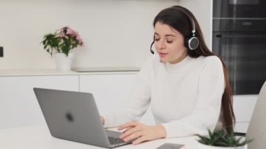 Kulaklıktaki kadın lider, projenin detaylarını Not Defteri üzerinden ekiple tartışıyor. Genç esmer kadın mutfakta masada oturuyor ve yavaş çekimde çalışıyor.