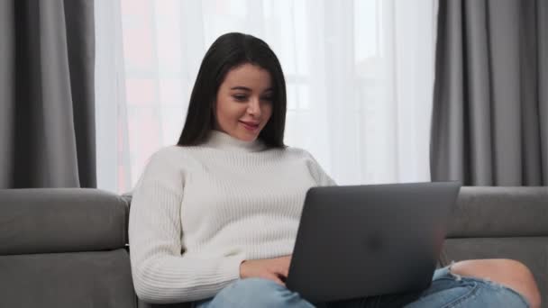 女学生很高兴在笔记本上看到考试成绩好 年轻的女人坐在沙发上 带着笔记本电脑 在客厅里感到快乐 — 图库视频影像