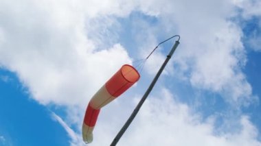Airport red and white windsock against blue sky with clouds. Vane shows direction and strength of wind