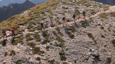 Tourists with backpacks go uphill exploring Italian Alps on sunny autumn day. Group of people walks on rocky mountain slope enjoying hiking aerial view