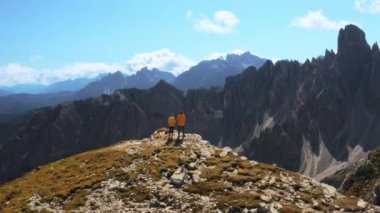 Tourist couple stands at edge of cliff looking at rocky mountain peak under blue sky. Woman and man enjoy exploring Alps backside view