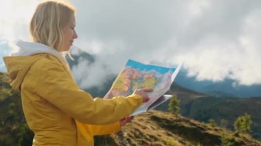 Curious woman studies map of Italian Alps pointing finger to mountain covered with dense fog. Blonde tourist hikes in highland on sunny day slow motion