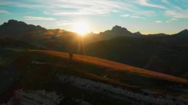 People contemplate bright sun setting behind giant mountains against cloudy sky. Tourists explore wildlife and nature of Italian Alps aerial view