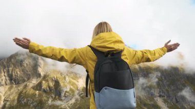 Happy female tourist spreads hands turning around in Italian Alps. Young woman with backpack feels happy to see Passo Giau pass in haze slow motion