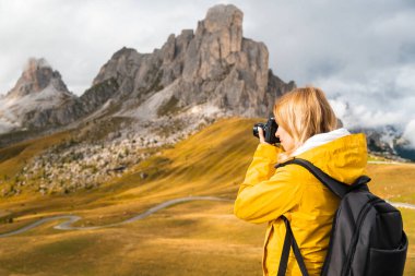 Professional photographer takes pictures of Passo Giau pass using camera. Woman with backpack enjoys activity in Italian Alps 