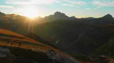 People with dogs walk on hill slope in giant mountains at sunset. Tourists enjoy hiking with animals in Italian Alps in evening aerial view